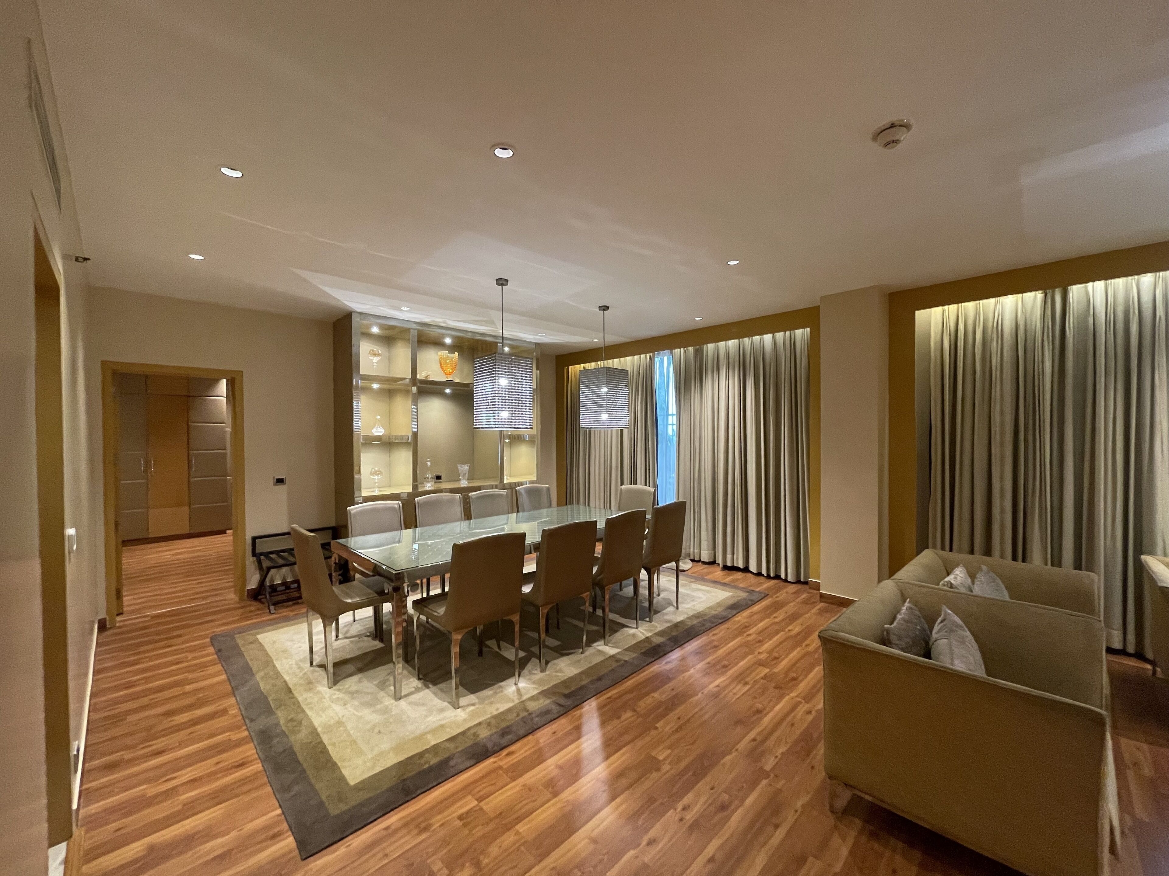 A modern dining area with a glass table and chairs, a chandelier, and a view of the city through large windows.