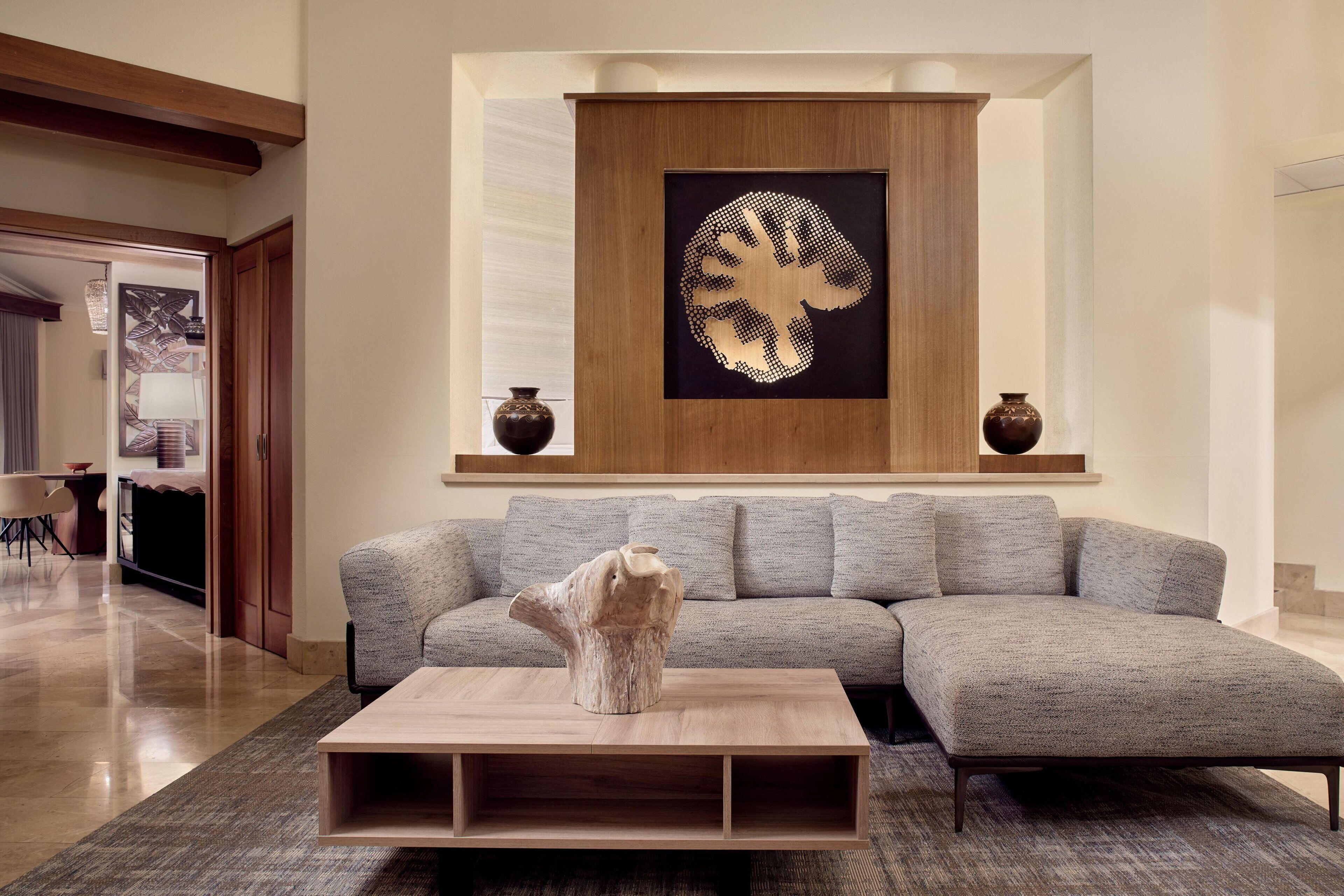 A modern living room with a sectional sofa, a wooden coffee table, and a decorative wall piece.
