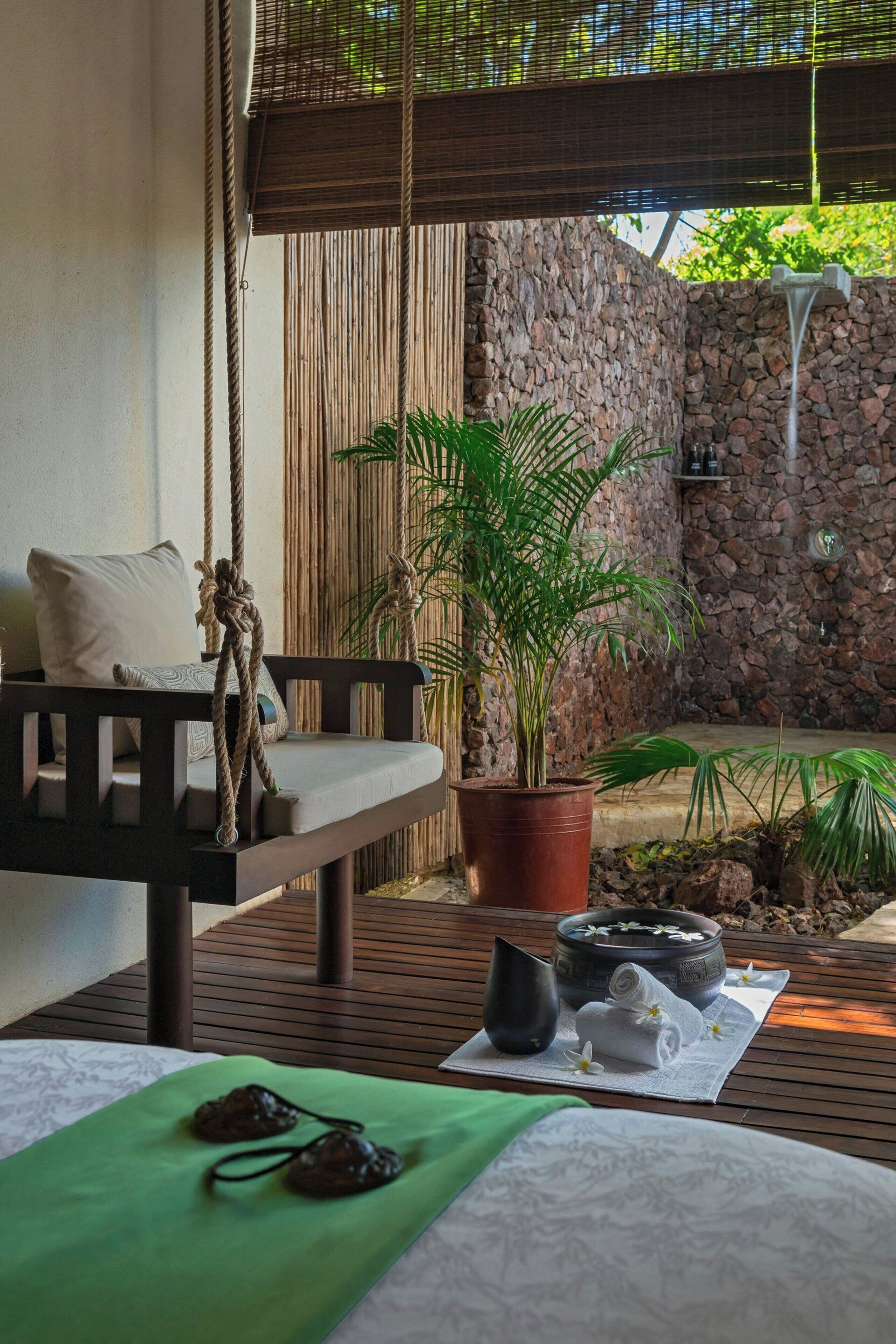 A spa area with a wooden bench, a potted plant, a stone wall, and a small waterfall feature.