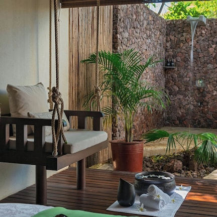 A spa area with a wooden bench, a potted plant, a stone wall, and a small waterfall feature.