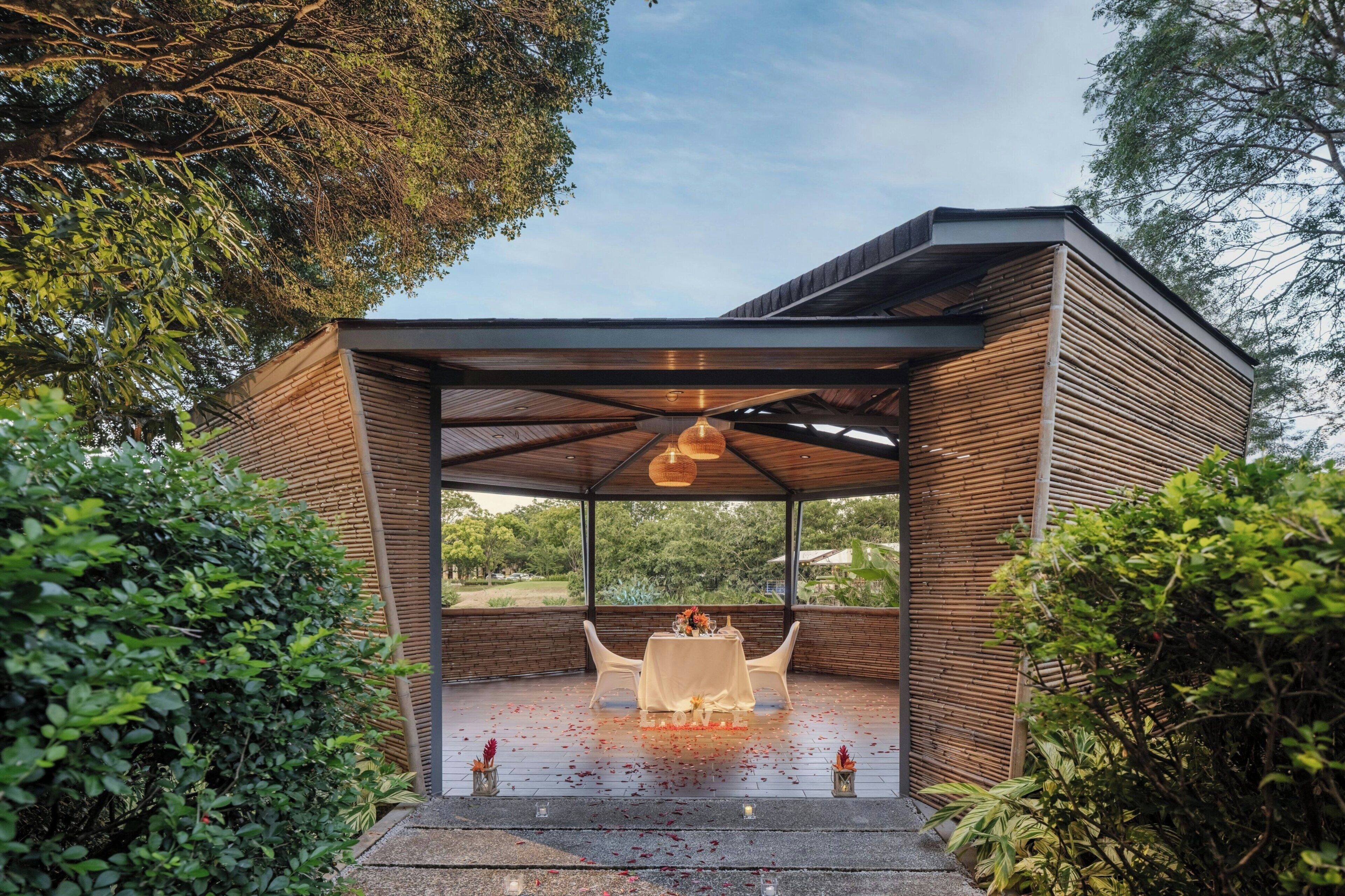 Un espace extérieur aménagé, abrité et doté d’une table et de chaises, entouré de verdure.