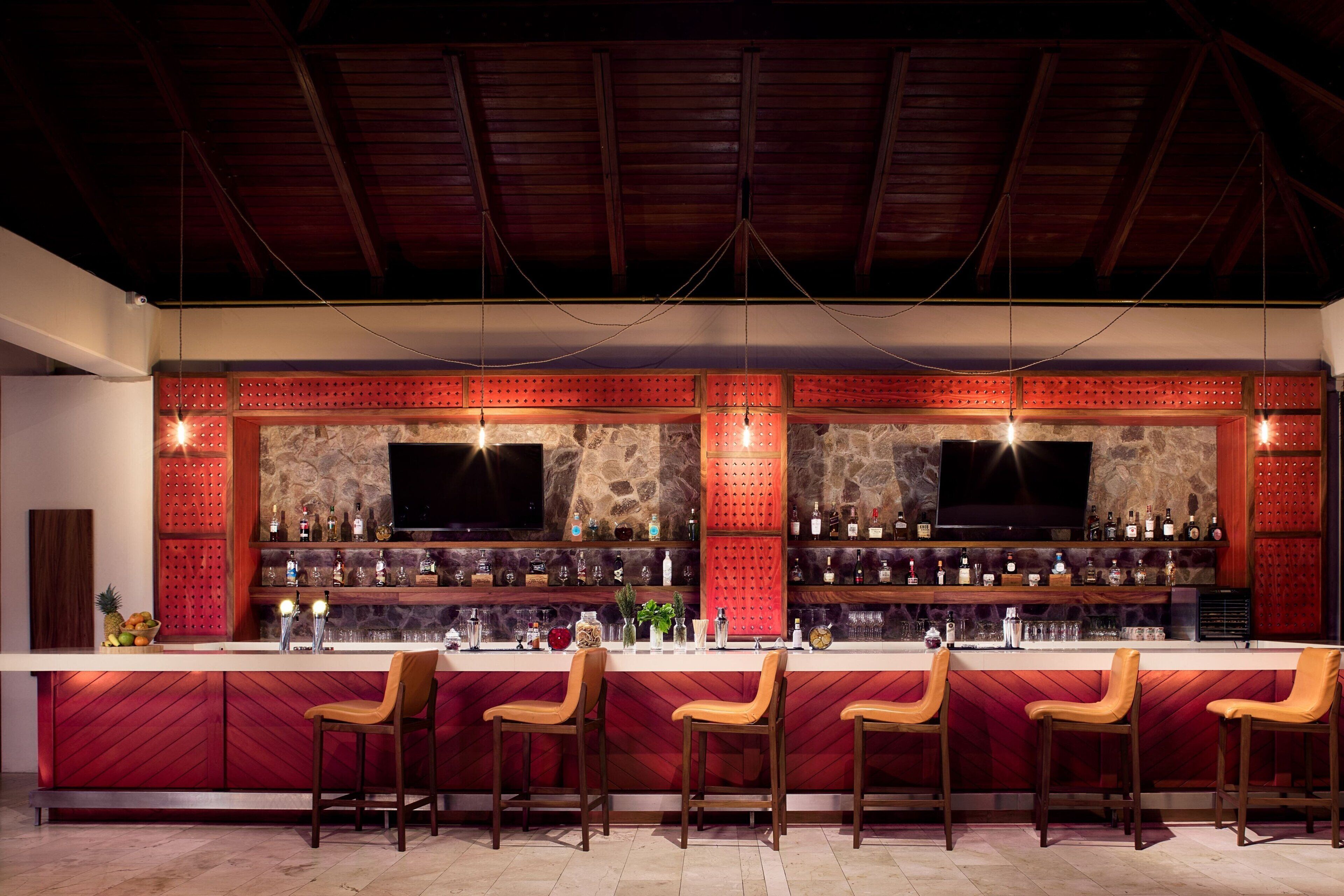 A bar area with a stone wall, wooden ceiling, and multiple bar stools.