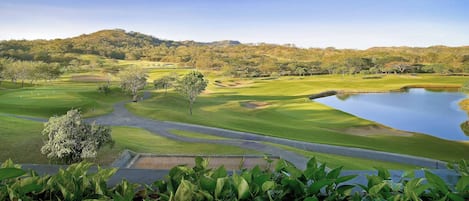 Um campo de golfe com lago, árvores e um cenário montanhoso.