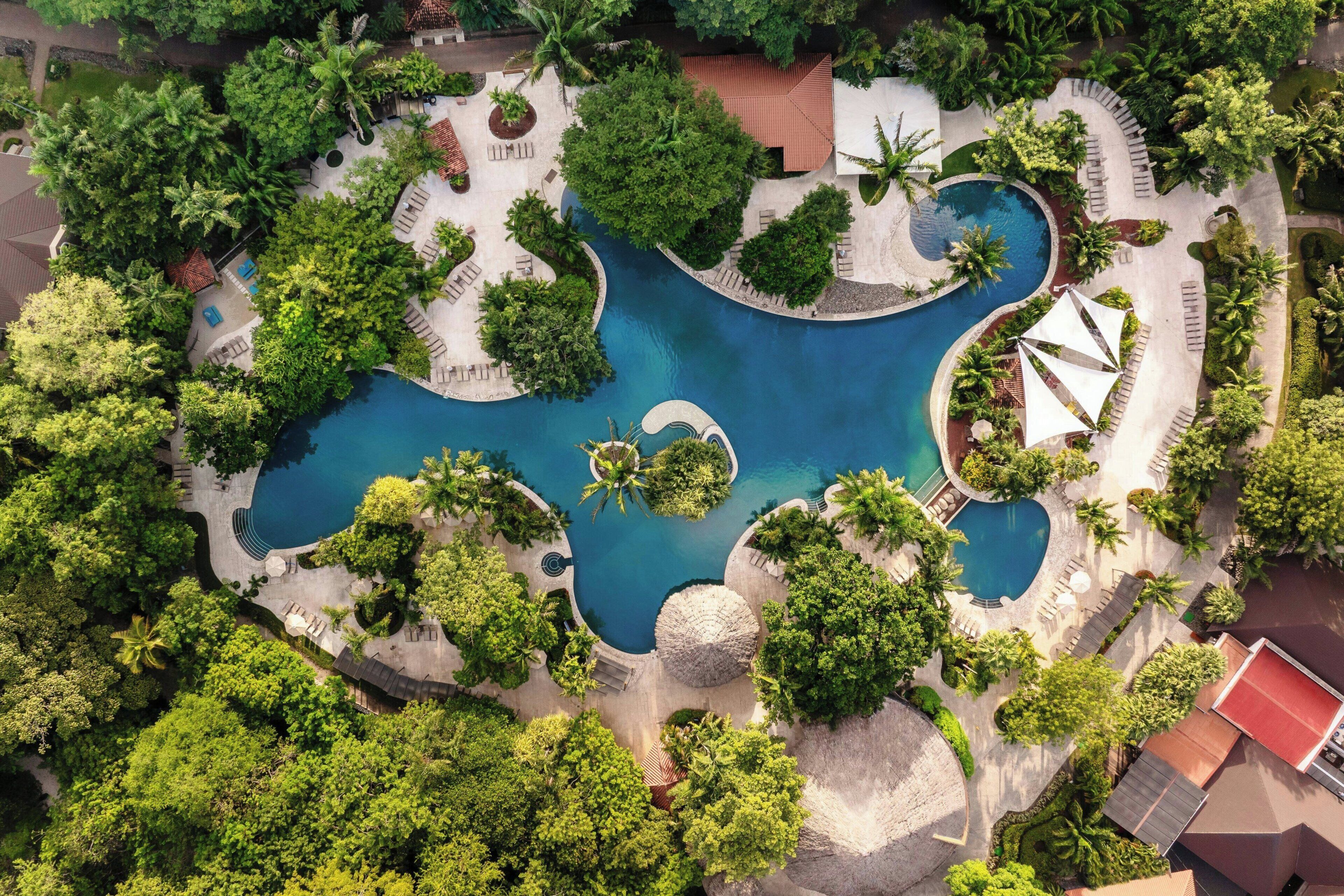 An aerial view of a resort with multiple swimming pools, lush greenery, and a variety of seating areas.