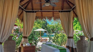 Relax in a serene space with a thatched roof, ceiling fan, and tranquil ambiance, perfect for unwinding near the pool.