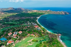 Vista aérea de um resort à beira-mar com vários edifícios, um campo de golfe e uma praia.