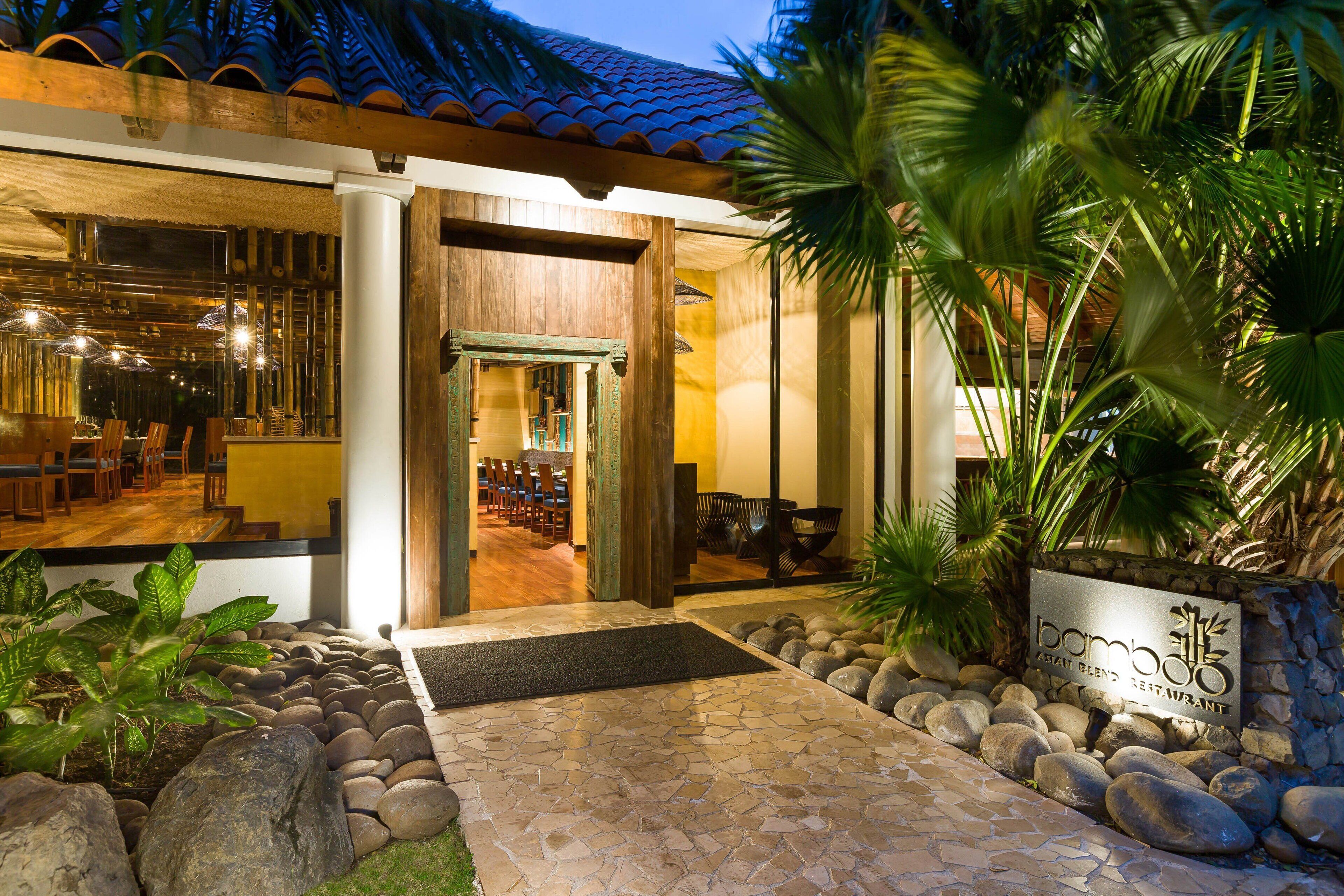 Entrada a un restaurante con un camino de piedra, una puerta de madera y un letrero que dice 'Bamboo Asian Blend Restaurant'.