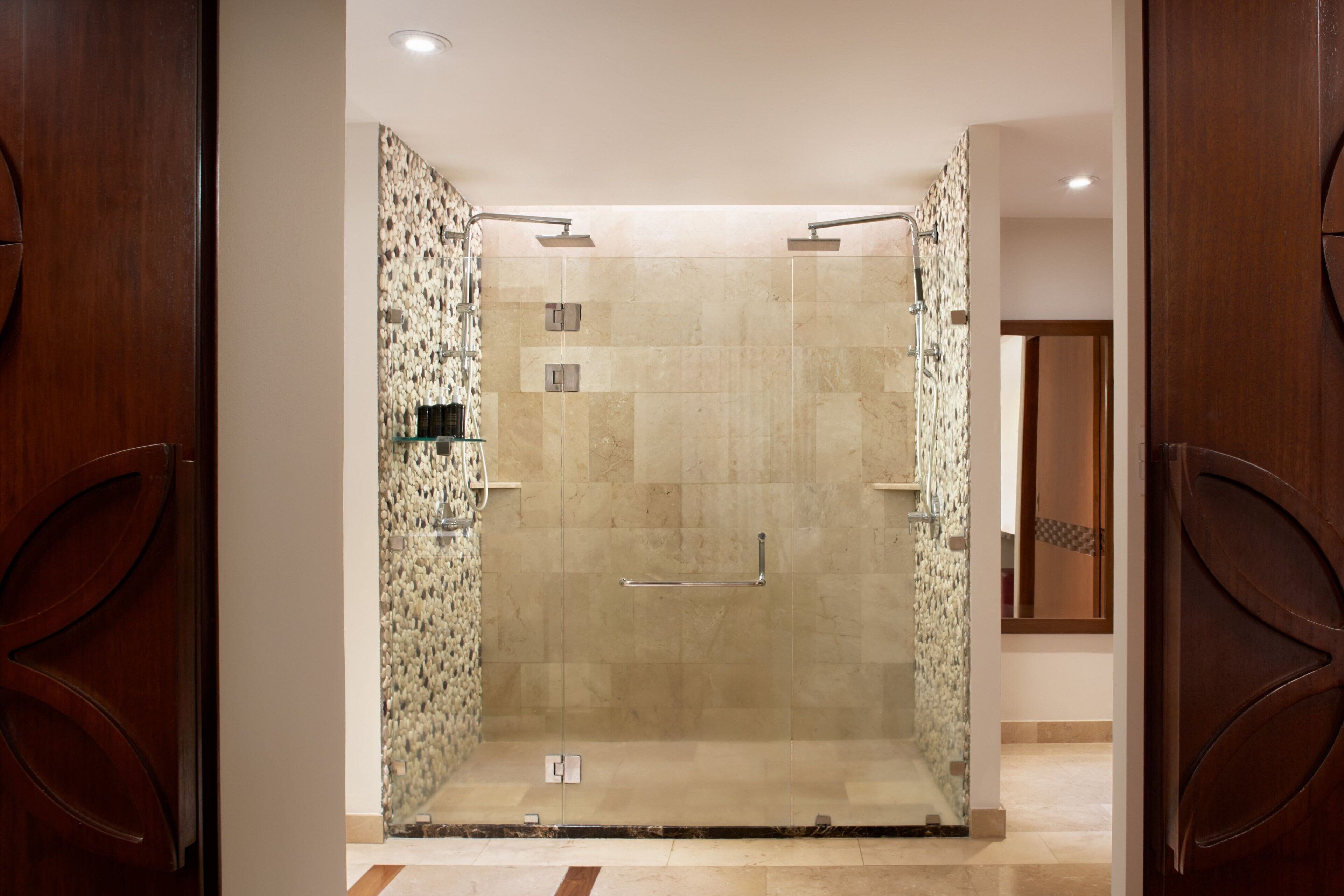 A glass-enclosed shower area with a tiled floor, a handrail, and a showerhead.