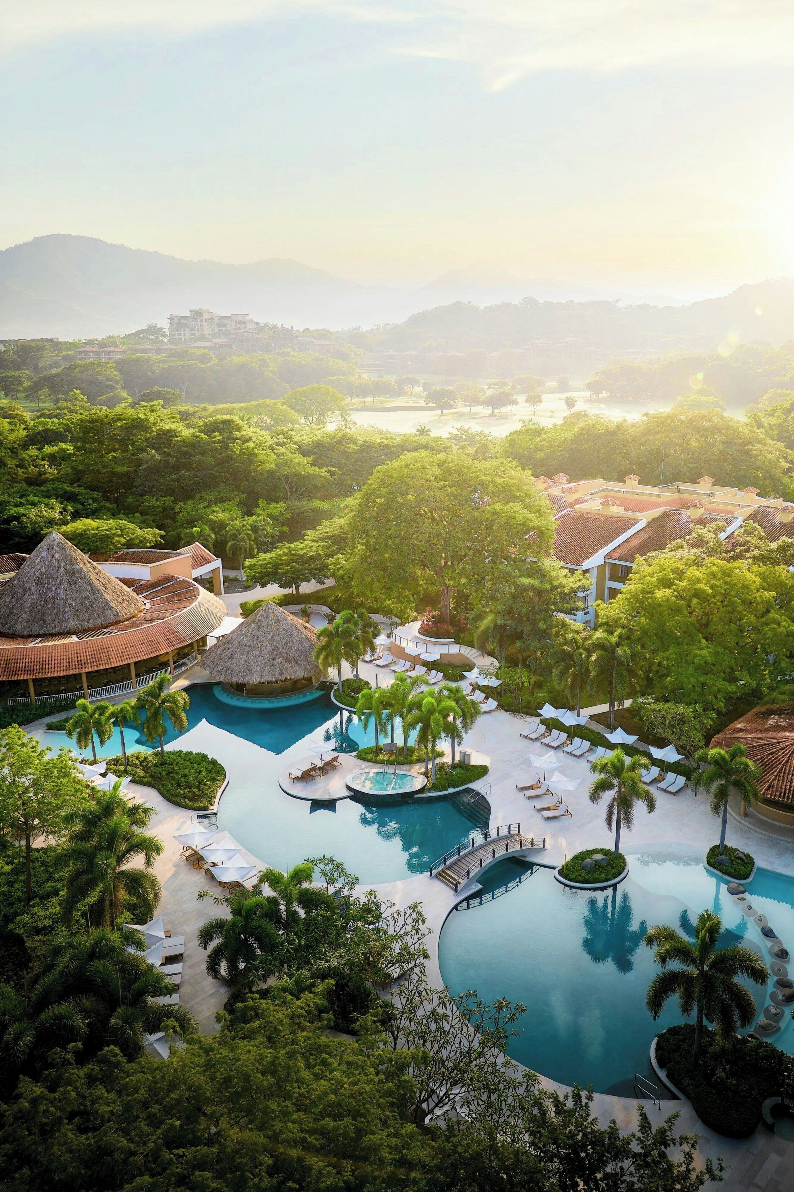 A resort with multiple swimming pools, palm trees, and thatched-roof structures.