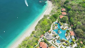 An aerial view of a resort with a beach, clear turquoise waters, and a swimming area with multiple pools. - The Westin Reserva Conchal, an All-Inclusive Golf Resort & Spa (Cabo Velas)