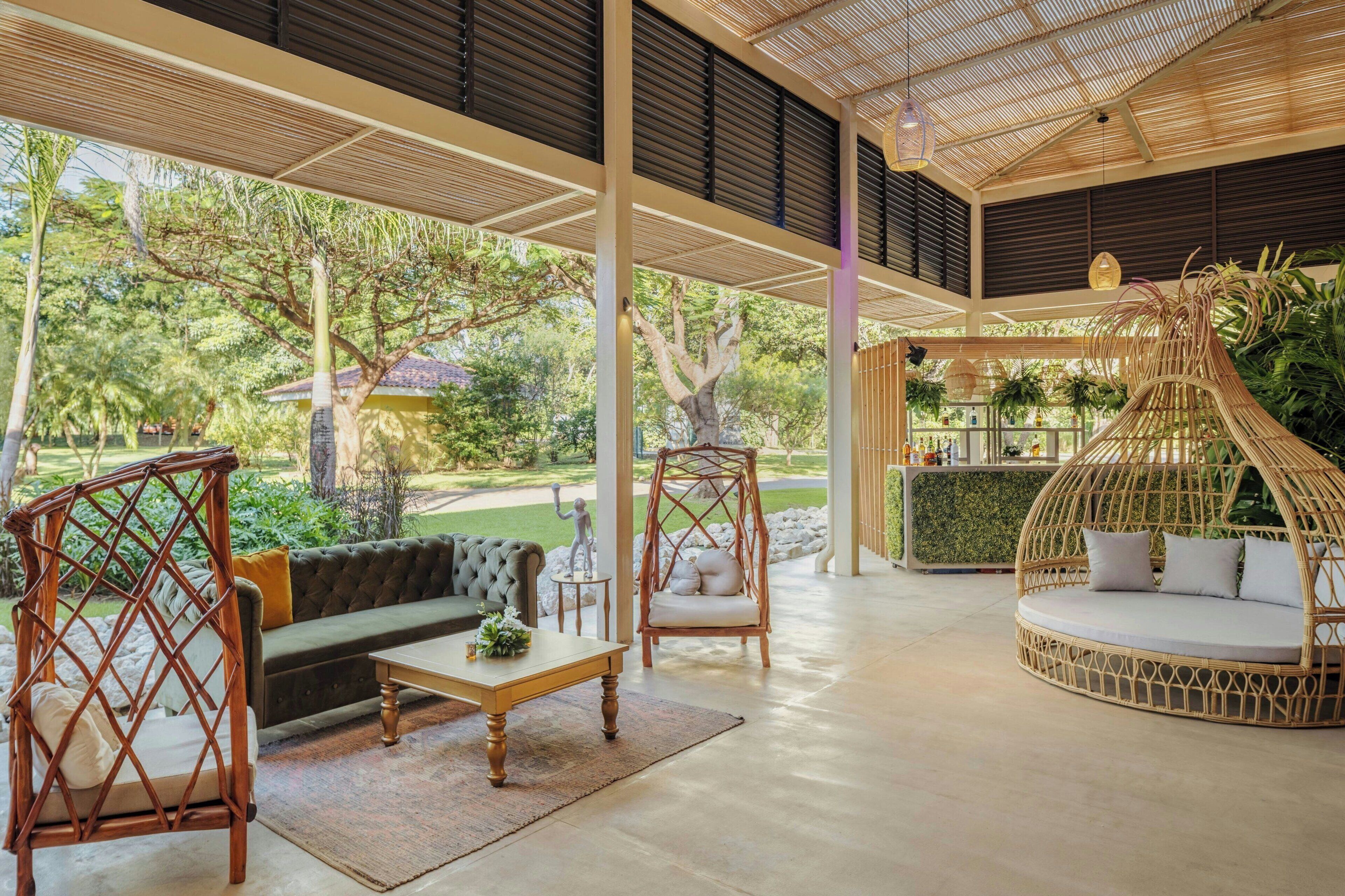 A spacious indoor area with a green sofa, a wooden coffee table, wicker chairs, and a round seating area.