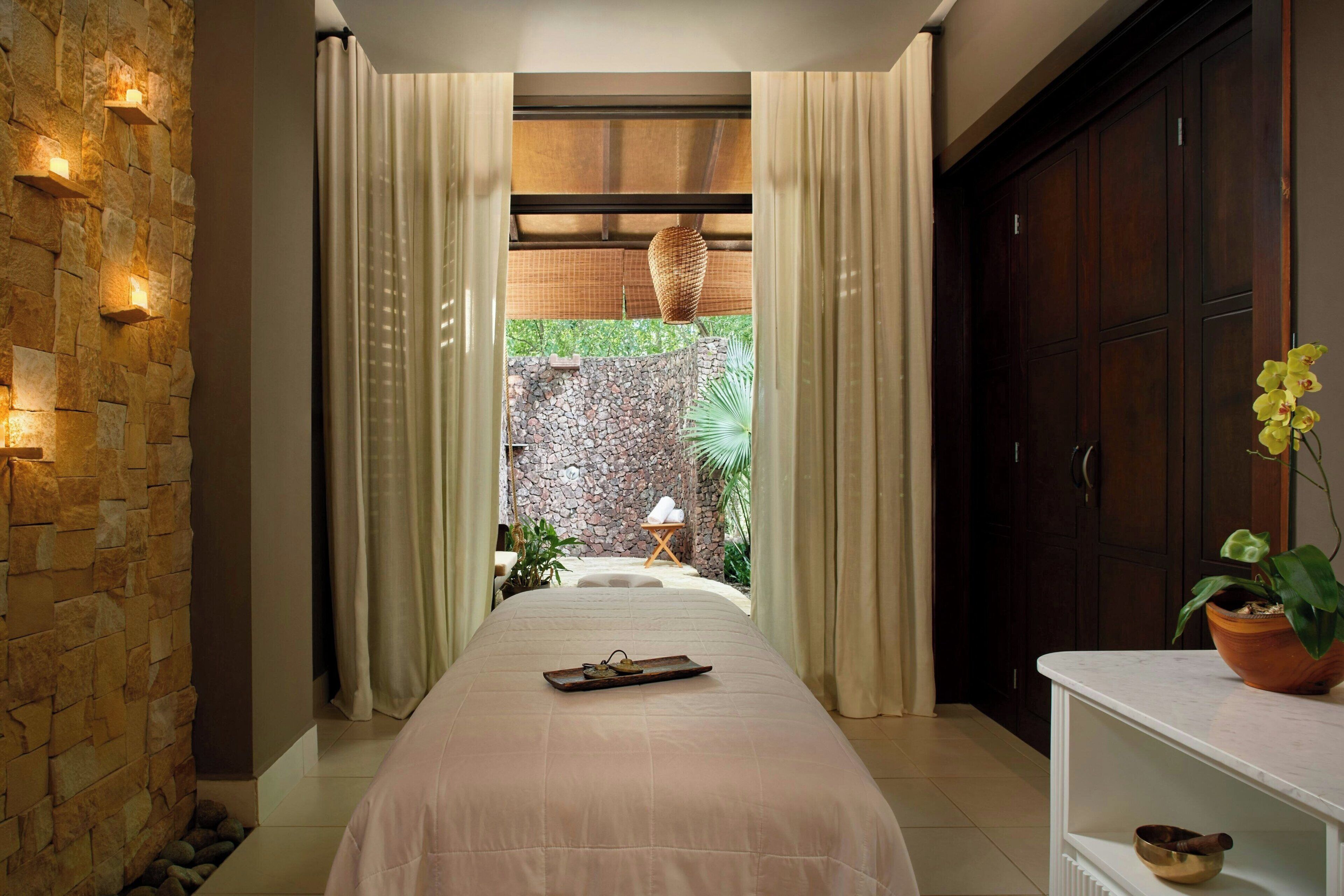 A bedroom with a stone wall, a bed with a tray, a wooden cabinet, and a view of an outdoor garden.