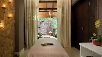 A bedroom with a stone wall, a bed with a tray, a wooden cabinet, and a view of an outdoor garden.