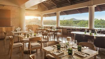 Un restaurante con mesas dispuestas para comer, amplias ventanas que ofrecen vistas al paisaje y un techo alto con vigas a la vista.