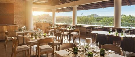 Un restaurante con mesas dispuestas para comer, amplias ventanas que ofrecen vistas al paisaje y un techo alto con vigas a la vista.