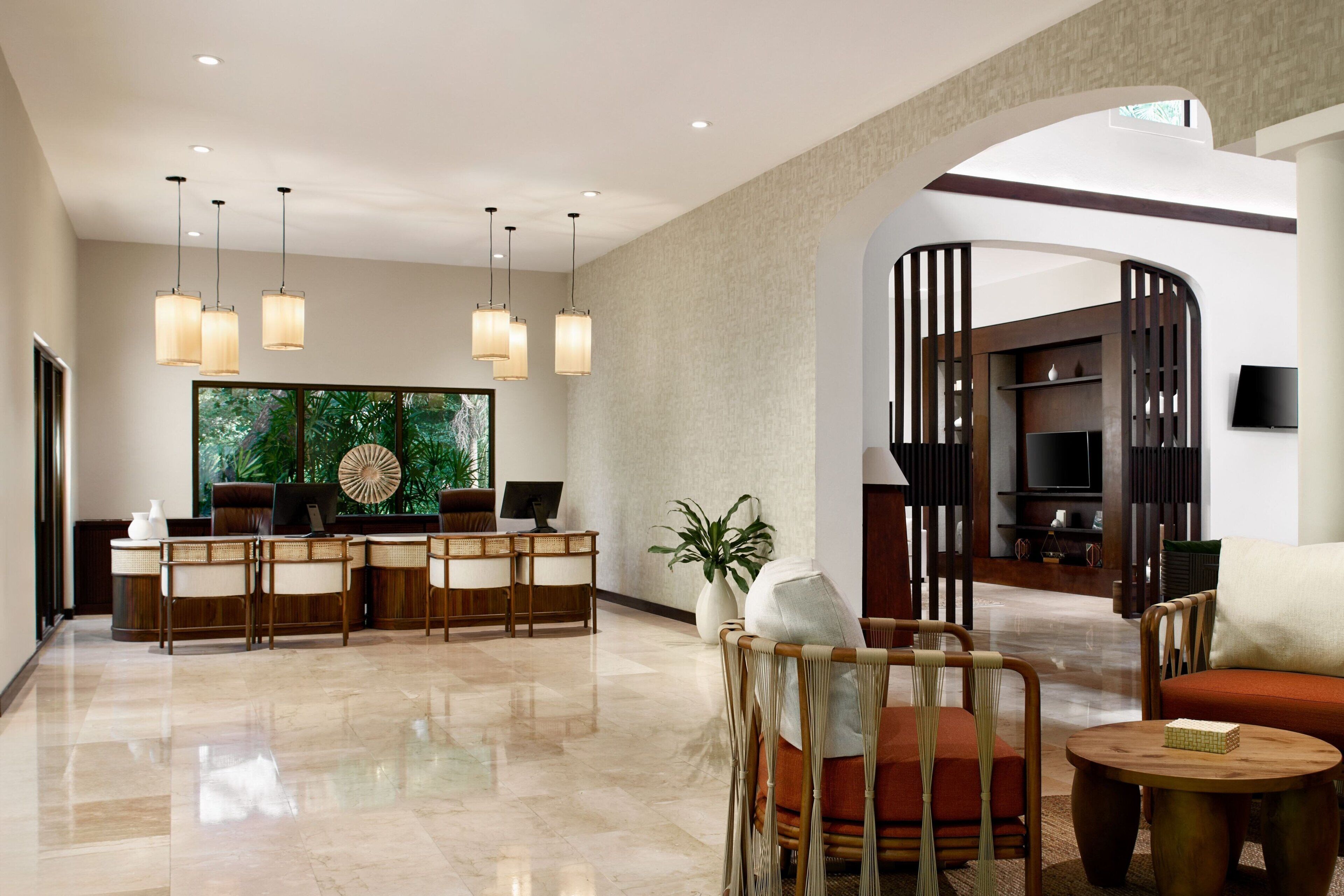 A spacious lobby with a reception desk, seating area, and a large window offering a view of greenery.