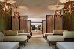 A modern hotel lobby with a central seating area, wooden flooring, and decorative hanging lights.