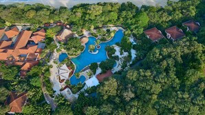 An aerial view of a resort with a central swimming pool, surrounded by lush greenery and beachfront properties.
