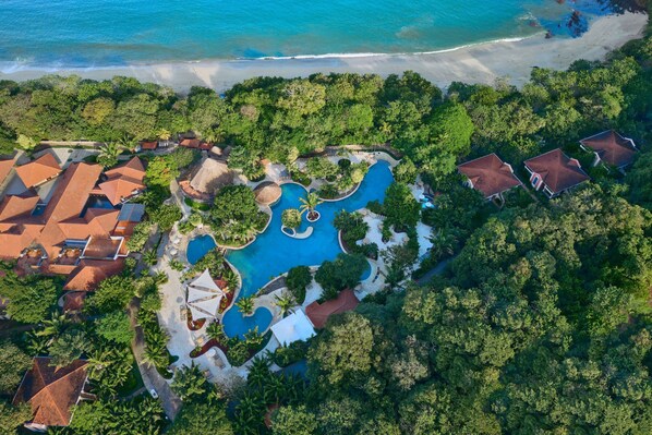 An aerial view of a resort with a central swimming pool, surrounded by lush greenery and beachfront properties. - The Westin Reserva Conchal, an All-Inclusive Golf Resort & Spa (Cabo Velas)