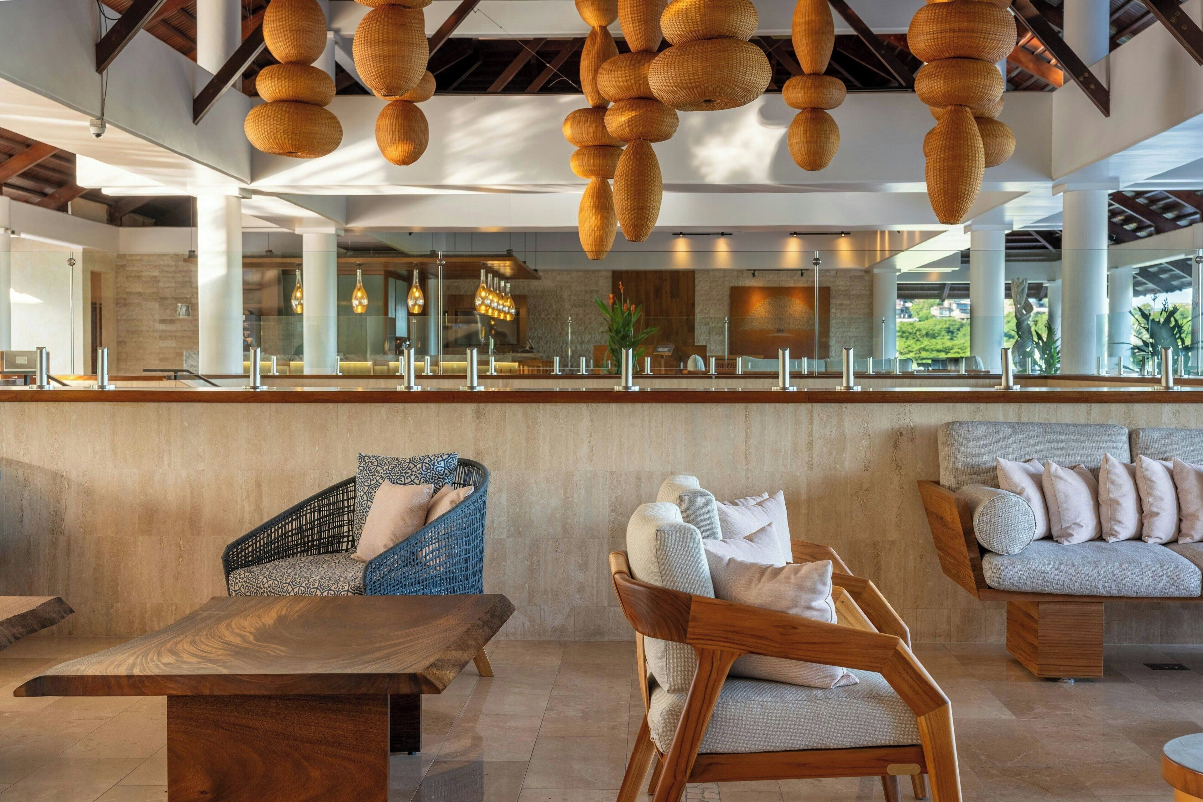 A modern lobby with a wooden reception desk, wicker chairs, and a sofa with cushions.