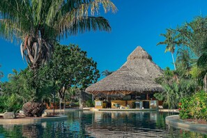Um resort com um edifício de telhado de palha, piscina e vegetação tropical exuberante.