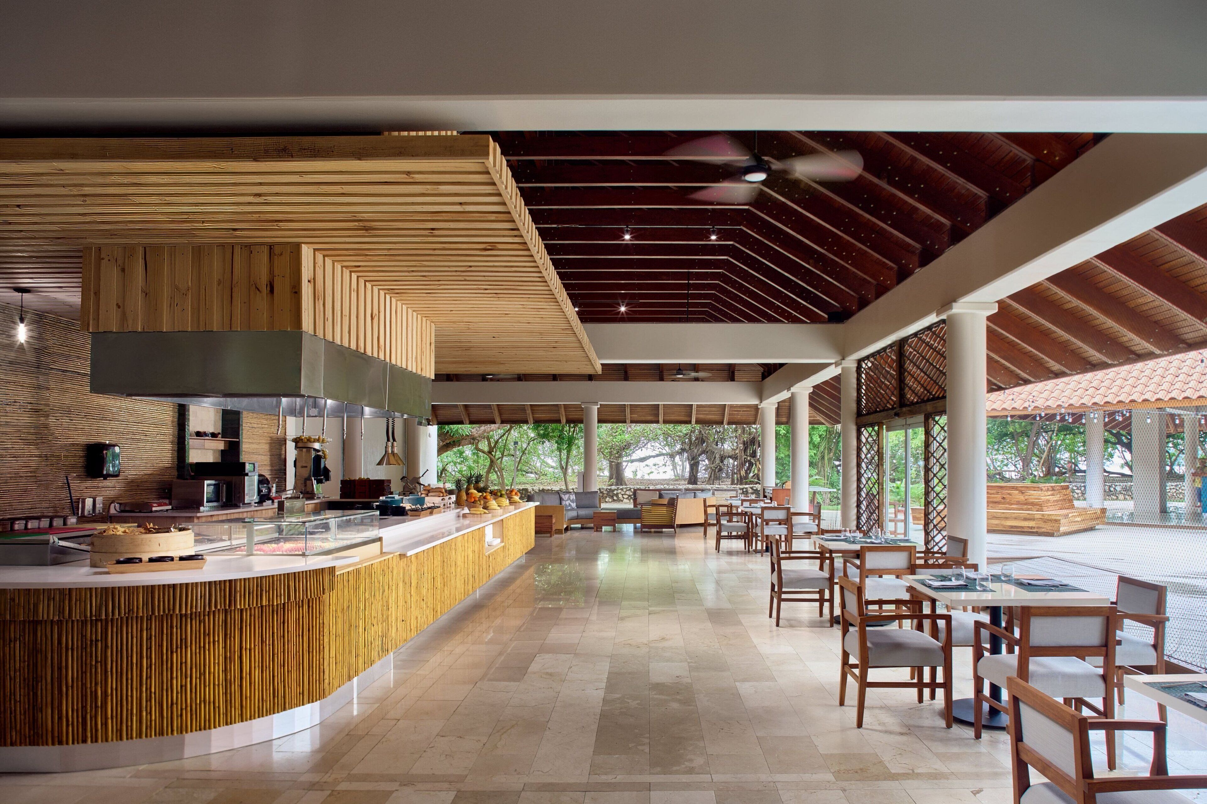 A modern restaurant with a wooden counter, seating area, and a ceiling with a geometric pattern.