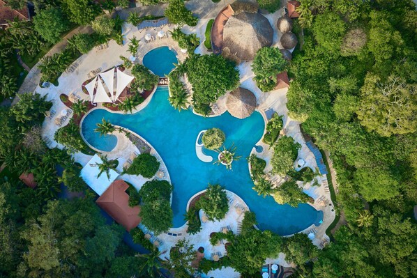 An aerial view of a resort with multiple swimming pools, palm trees, and thatched-roof structures. - The Westin Reserva Conchal, an All-Inclusive Golf Resort & Spa (Cabo Velas)