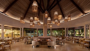 A spacious indoor area with multiple dining tables and chairs, a central seating area, and large windows offering views of the outdoors.