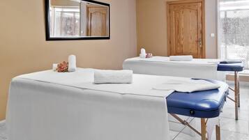 Un cuarto de spa con dos camillas de masaje, una puerta de madera y un espejo en la pared.