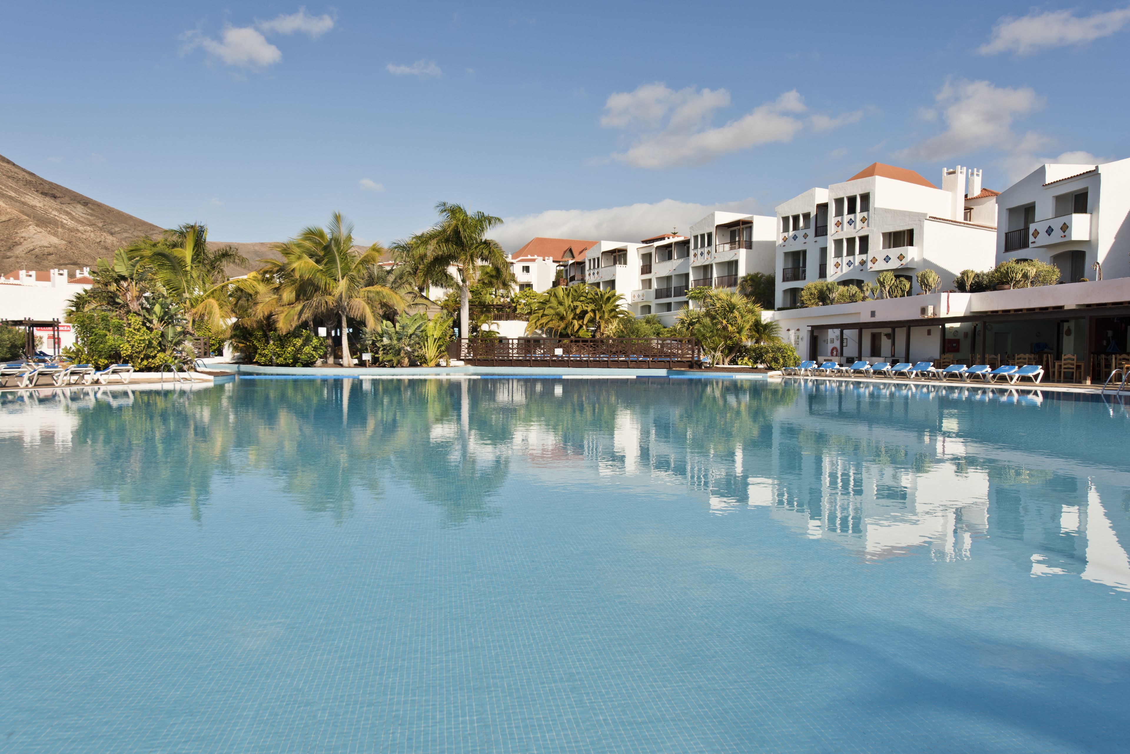 A swimming pool with lounge chairs, palm trees, and a building with balconies.