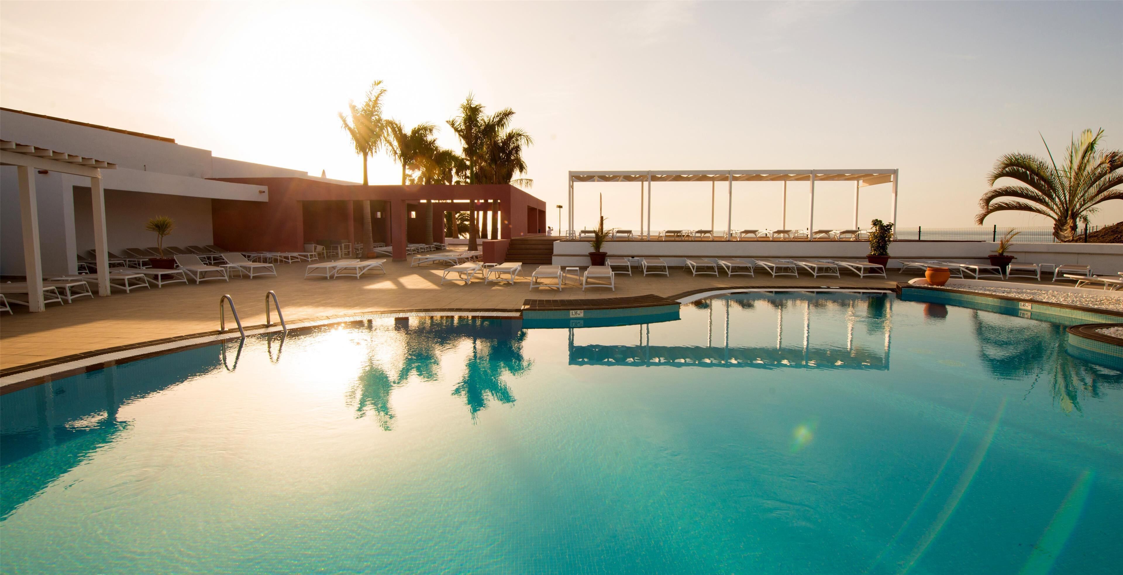 A pool area with lounge chairs and a building with a covered seating area.