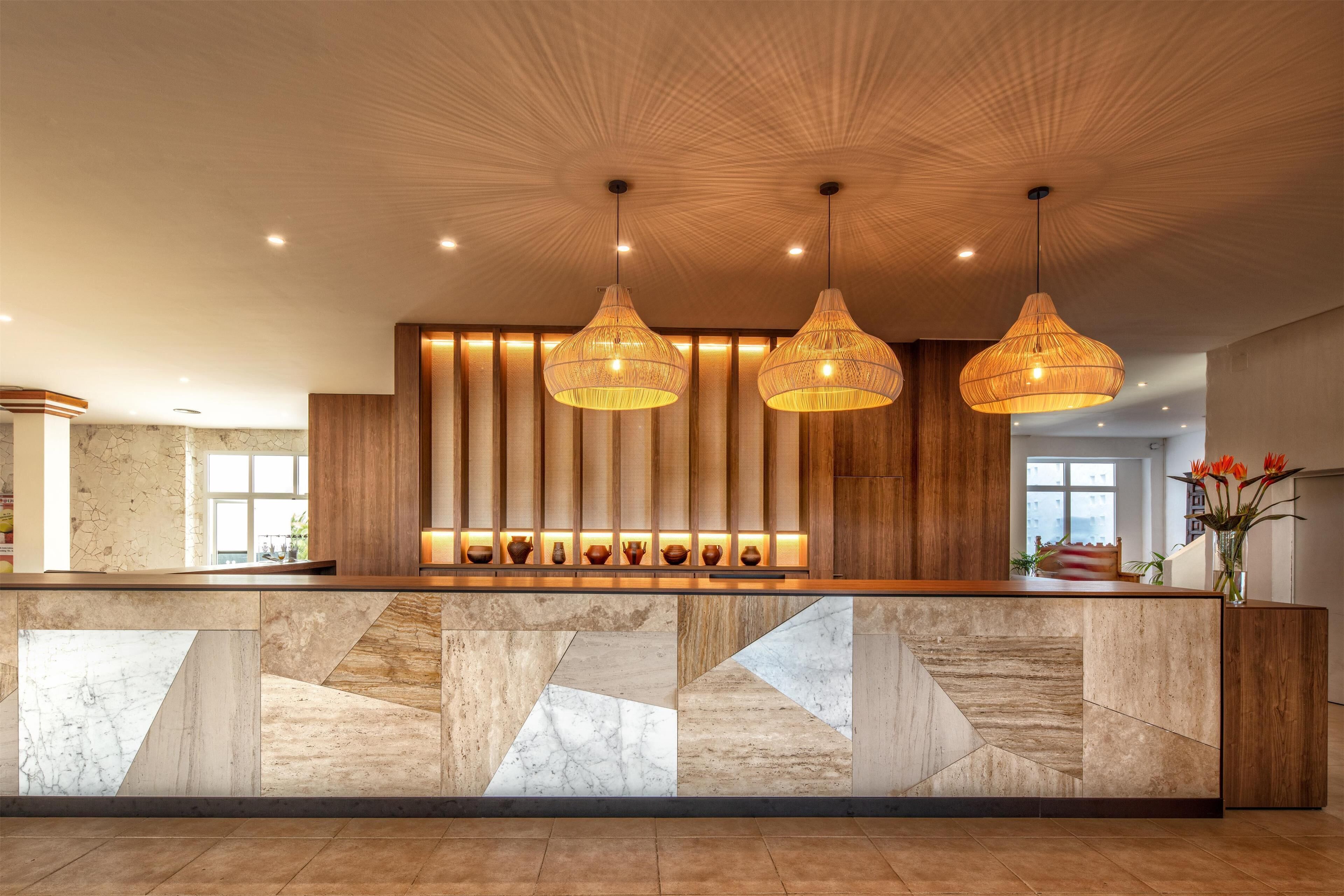 A reception area with a wooden counter, geometric tile design, and hanging wicker pendant lights.