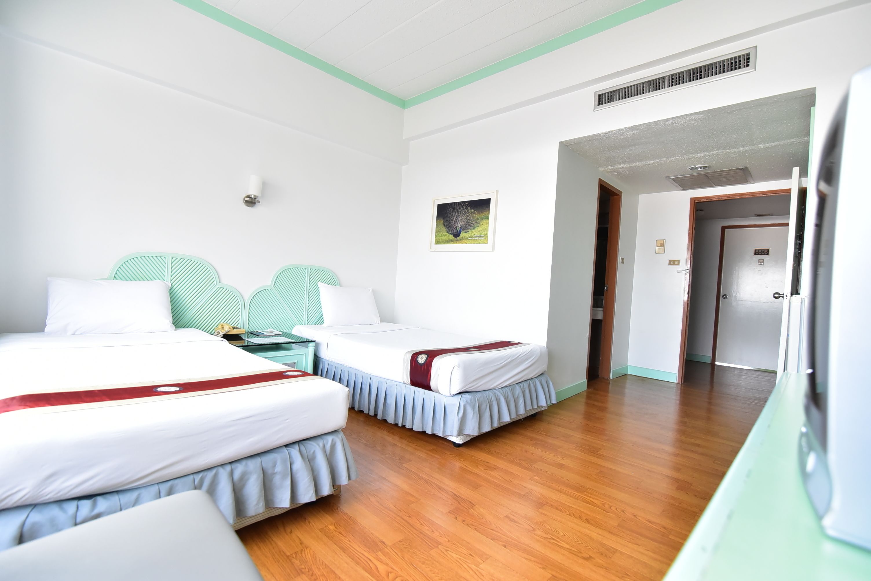 A hotel room with two beds, a wooden floor, a green accent wall, and a door leading to another room.