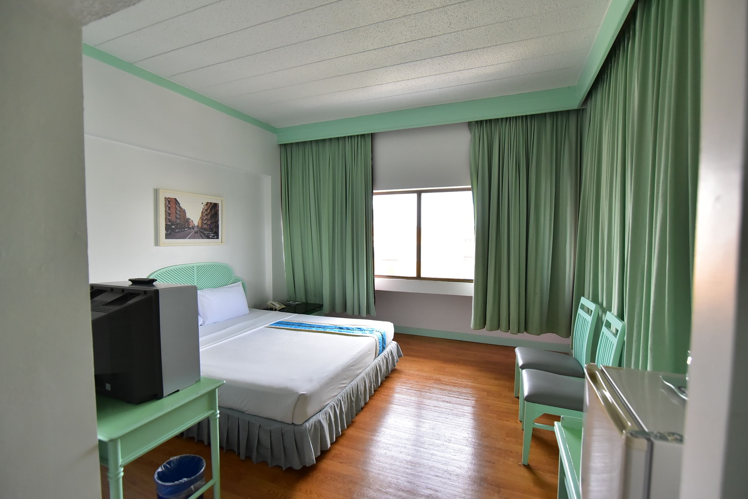 A hotel room with a bed, a desk with a computer, a chair, and a window with curtains.