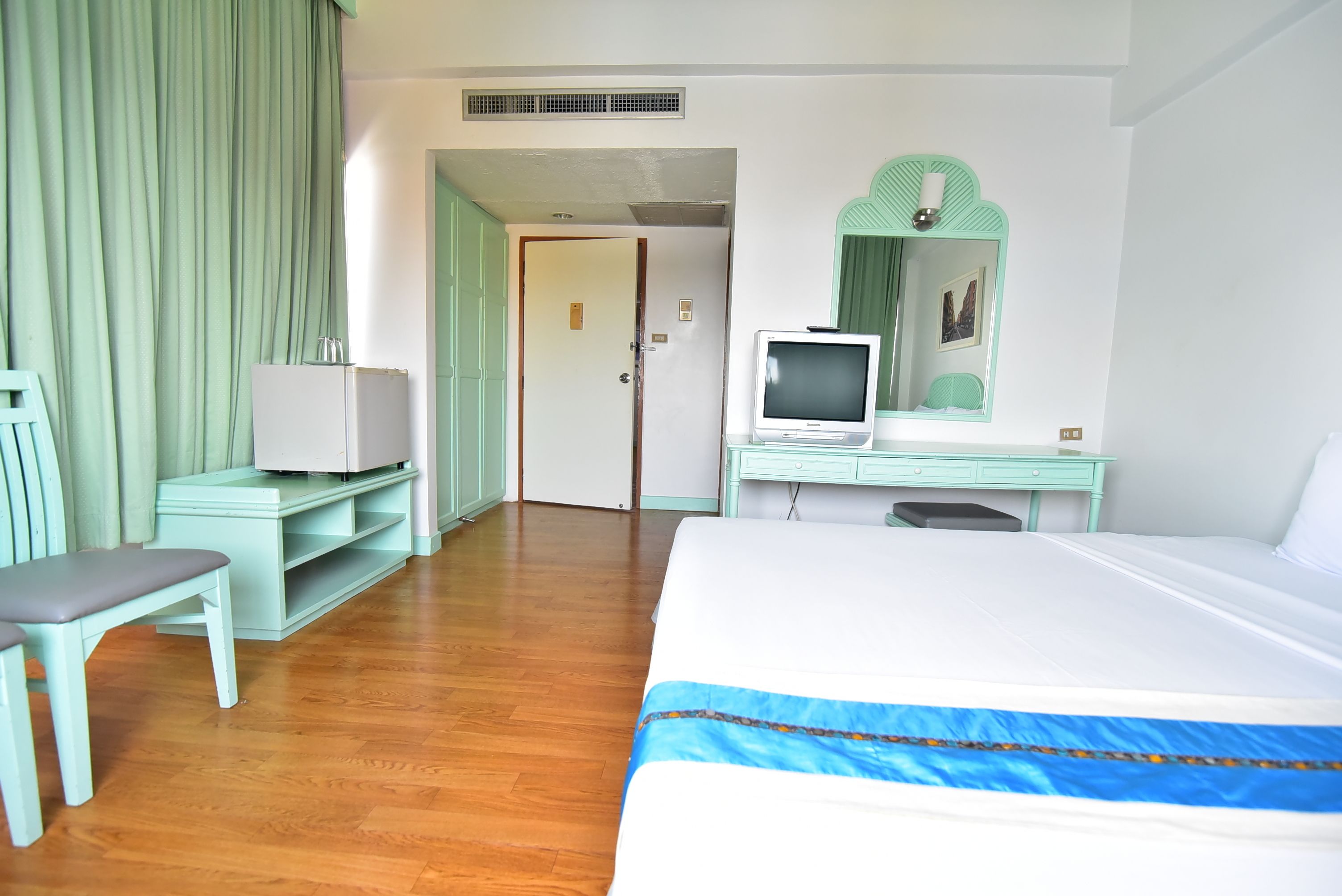 Una habitación de hotel con una cama, un escritorio con televisor, una silla y un espejo.