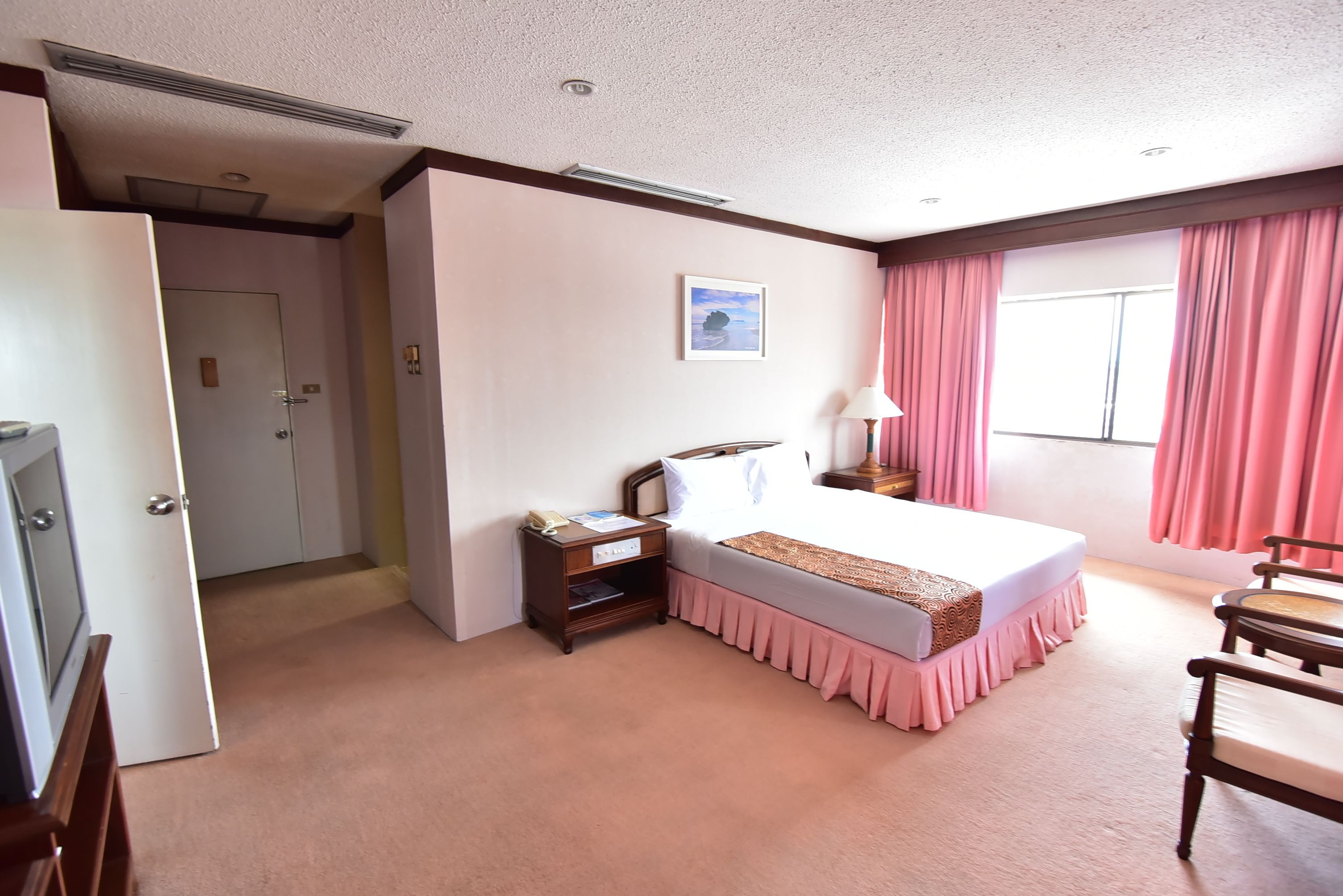 A hotel room with a bed, bedside table, lamp, and a window with curtains.