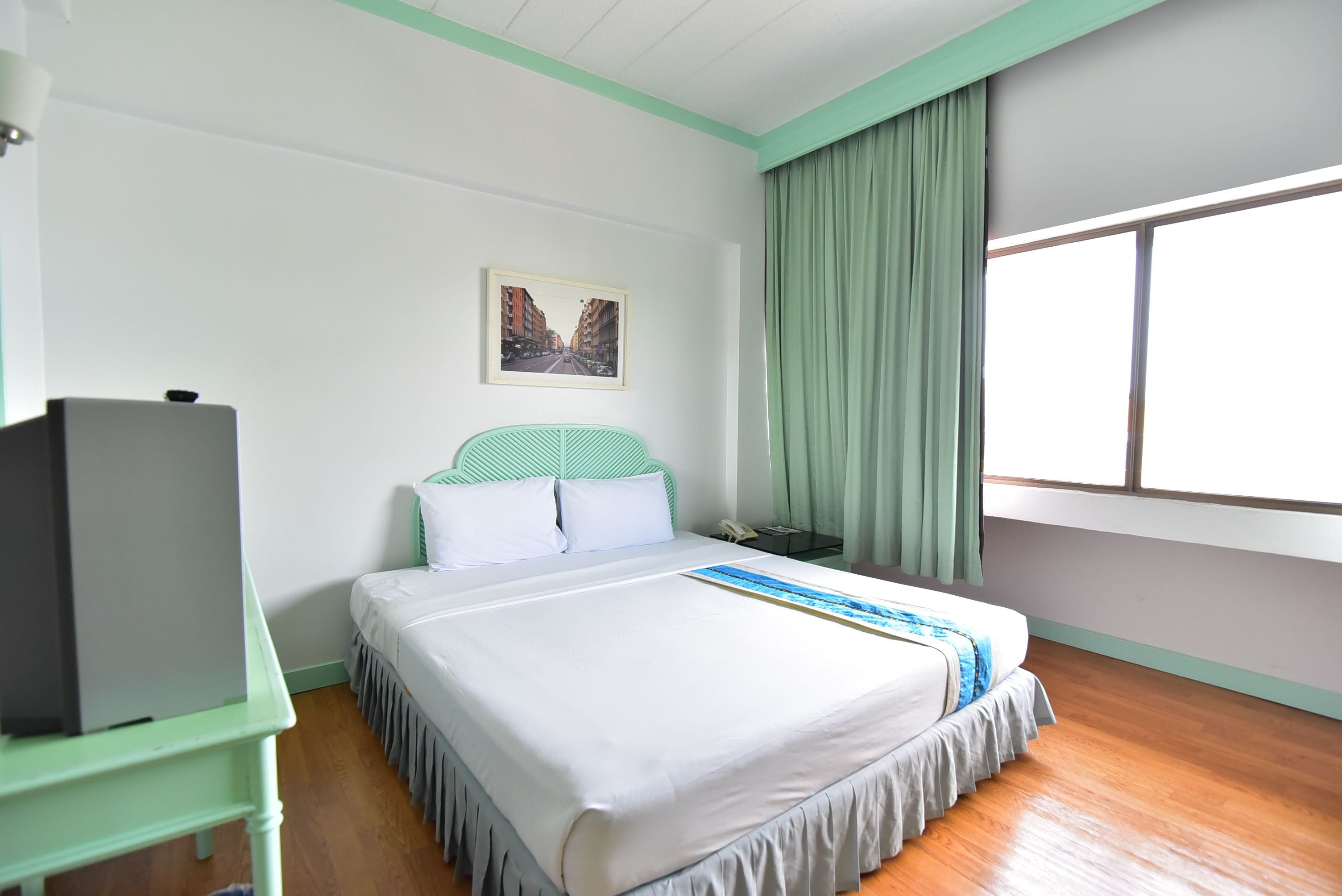 Una camera d'hotel con un letto, una scrivania, una televisione, una finestra con tende e un quadro appeso al muro.