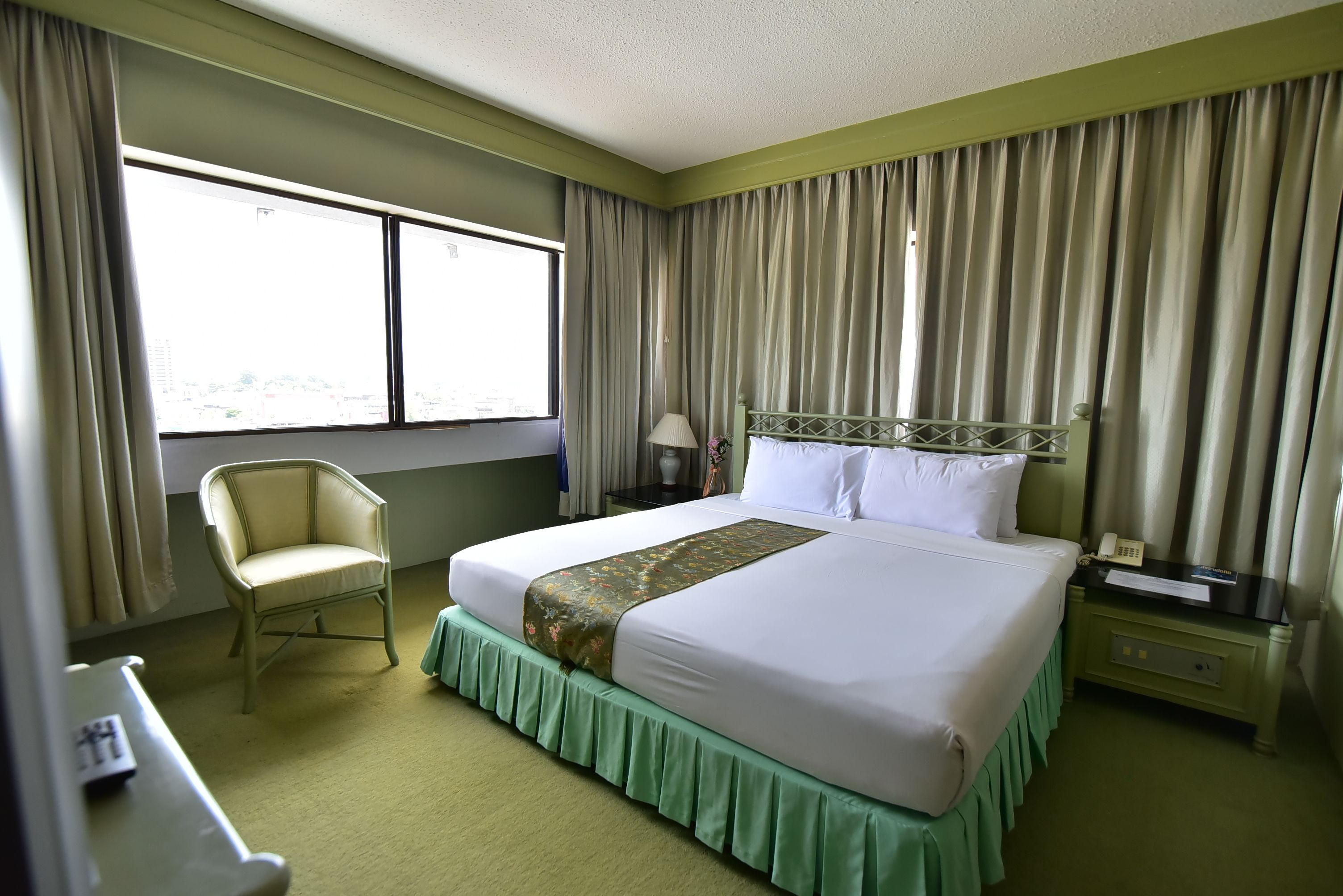 Een hotelkamer met een bed, een stoel, een nachtkastje en een raam met gordijnen.