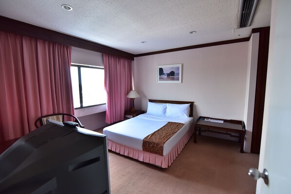 Una habitación de hotel con cama, escritorio, silla, mesita de noche y ventana con cortinas.