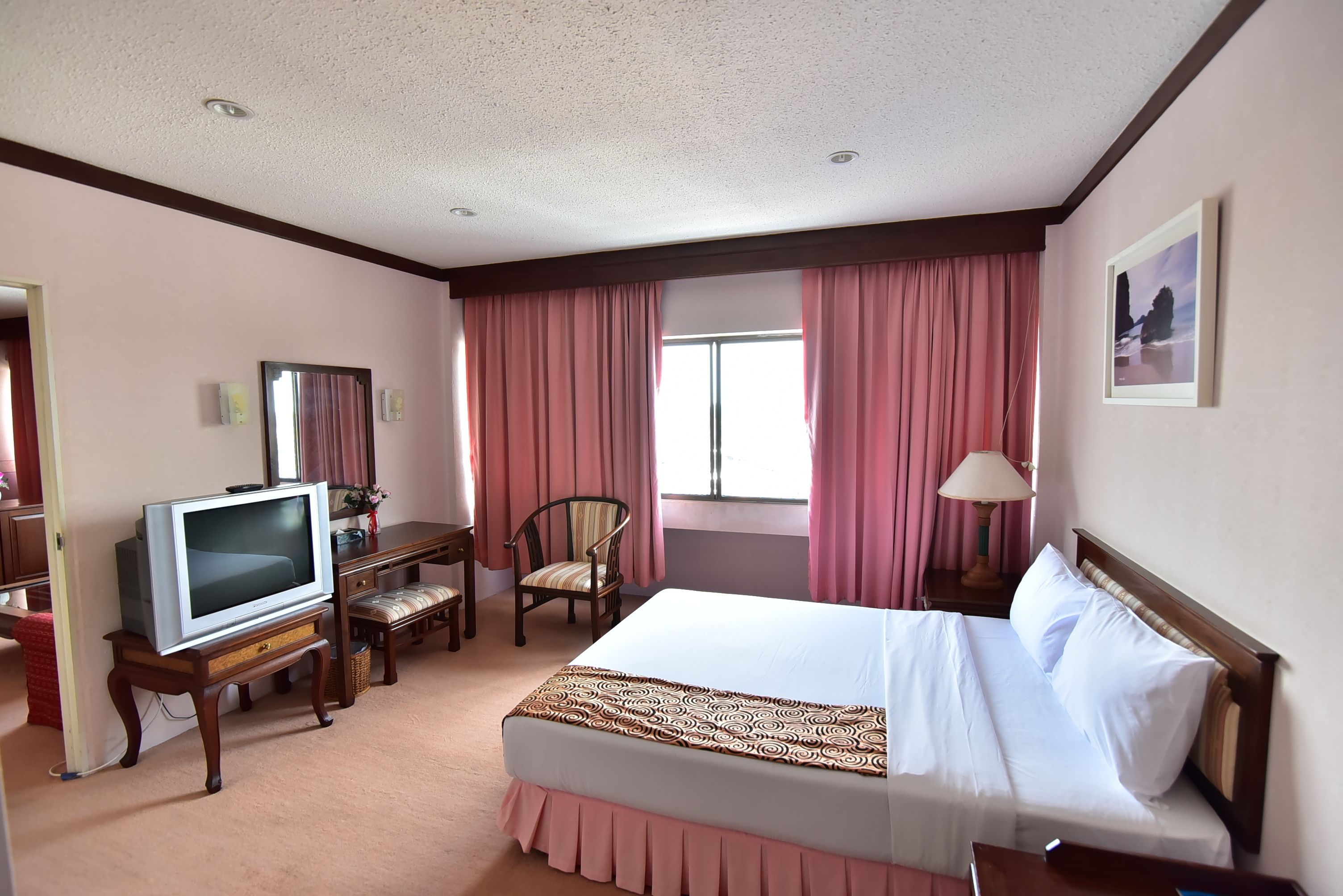 A hotel room with a bed, a desk with a chair, a television, and a window with curtains.