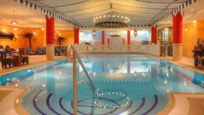 Una piscina interior con una fuente central, rodeada de sillones de descanso y una barandilla decorativa.