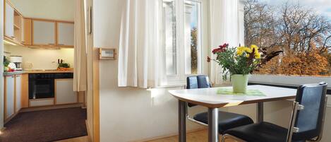 A modern kitchen with wooden cabinets, a dining area with a table and chairs, and a view of trees through a window.