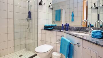 Une salle de bain moderne avec une douche à parois de verre, des toilettes blanches, un lavabo agrémenté de serviettes bleues et un miroir avec un porte-serviettes.