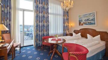 A hotel room with a bed, a desk, a chair, a table, and a balcony with curtains.