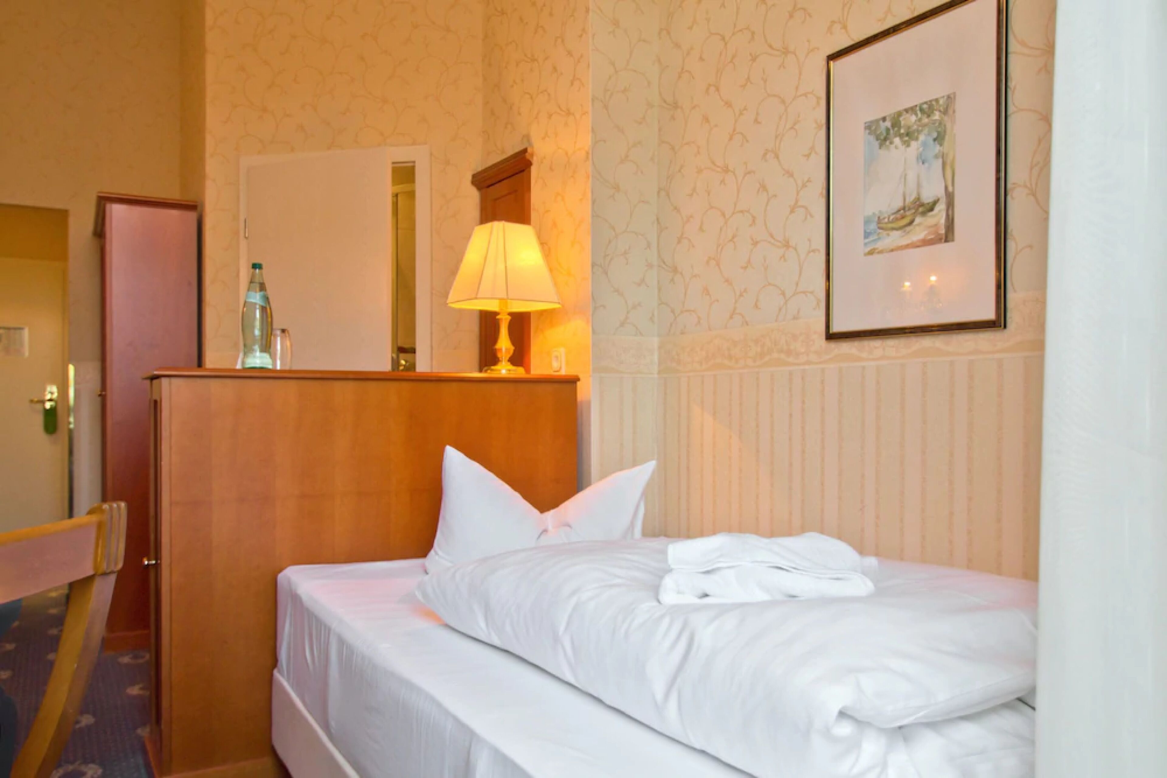 A hotel room with a neatly made bed, a bedside lamp, a mirror, and a framed picture on the wall.
