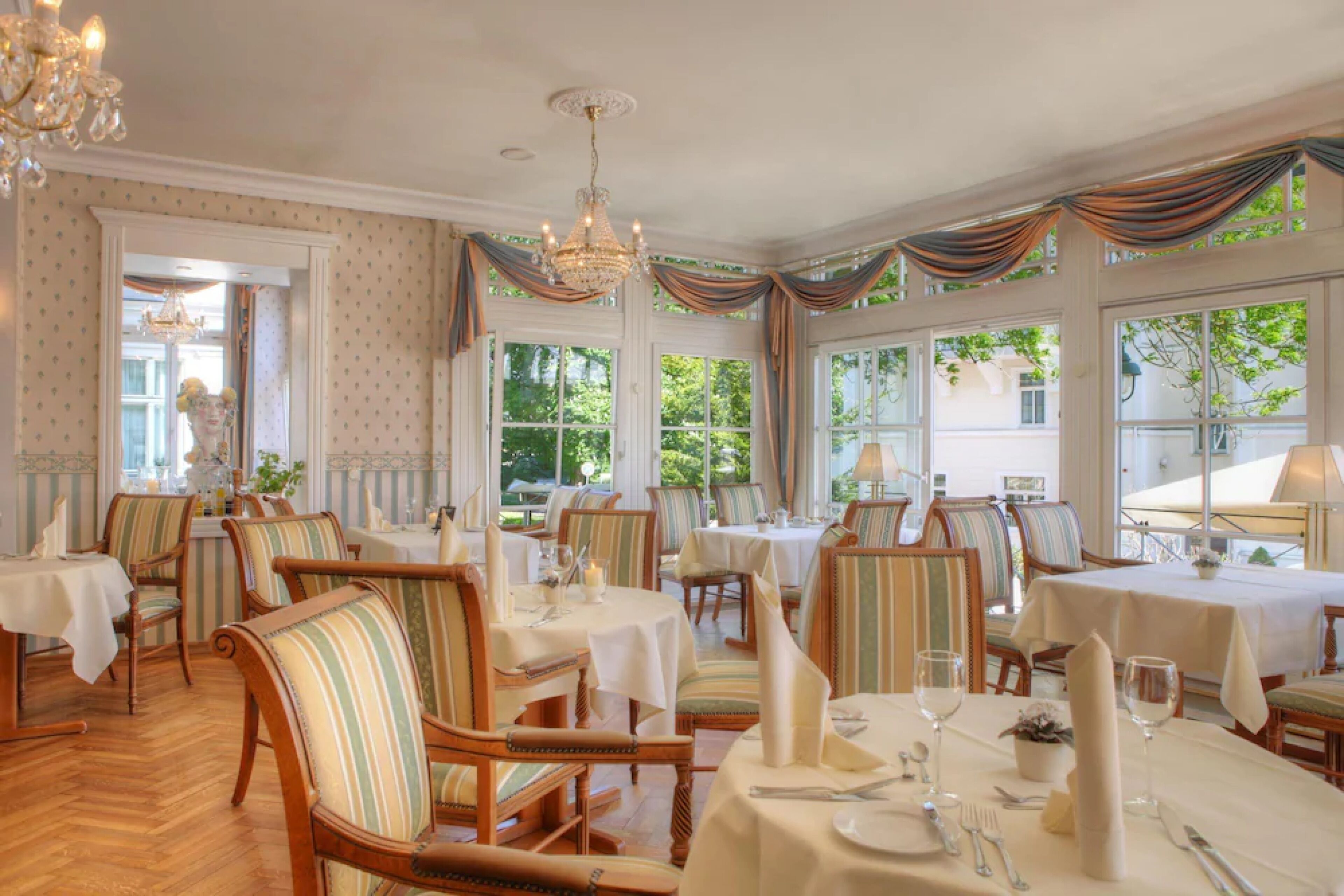 Un comedor con sillas tapizadas a rayas, mesas redondas y candelabros.