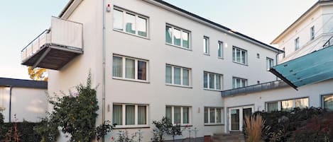 Un edificio residencial de varios pisos con tejado plano, ventanas amplias y un pequeño balcón.