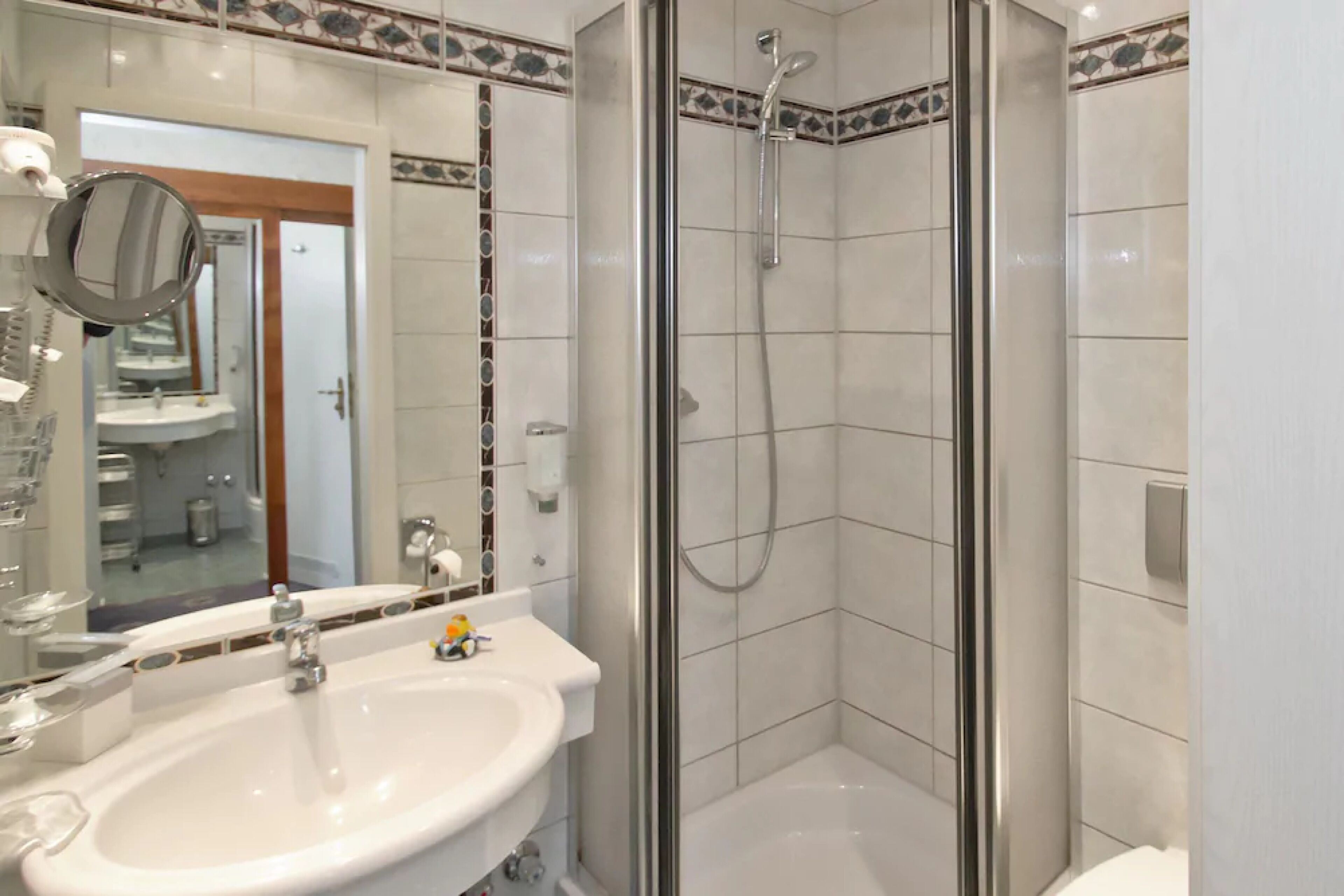 Une salle de bain avec une douche à parois de verre, un lavabo avec un miroir et un sol carrelé.