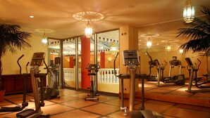 Un gimnasio con diversas máquinas de ejercicio, piso de madera e iluminación decorativa.