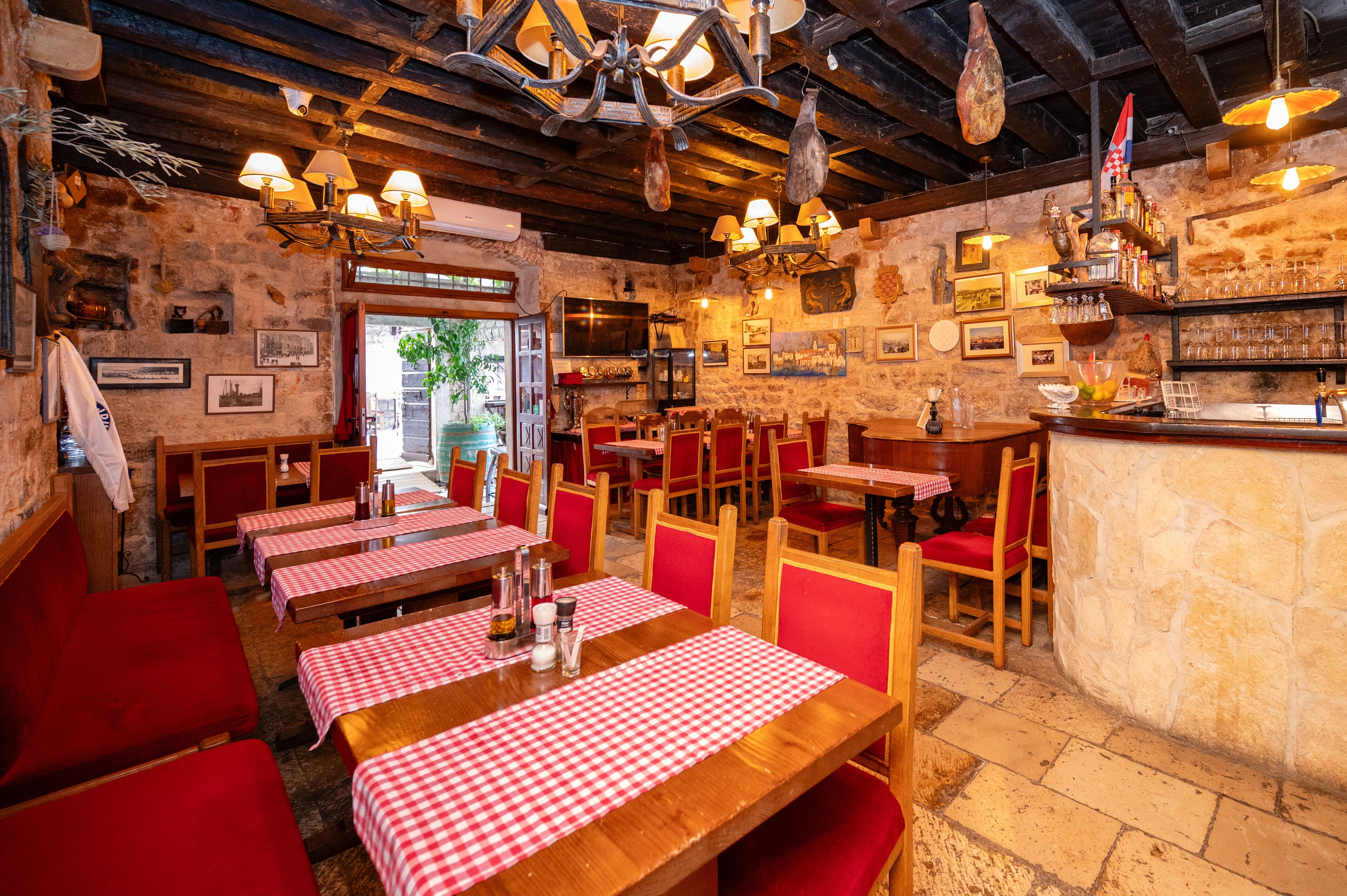 A rustic restaurant with wooden tables and red chairs, stone walls, and a bar area.